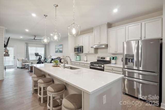 kitchen featuring a kitchen island with sink, appliances with stainless steel finishes, a sink, open floor plan, and under cabinet range hood