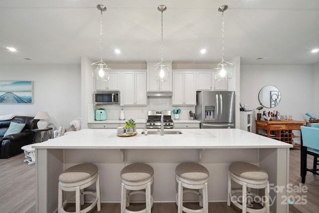 kitchen with a kitchen breakfast bar, appliances with stainless steel finishes, an island with sink, and light wood-type flooring