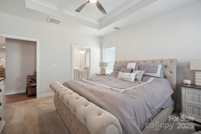 bedroom with visible vents, light carpet, baseboards, connected bathroom, and a raised ceiling