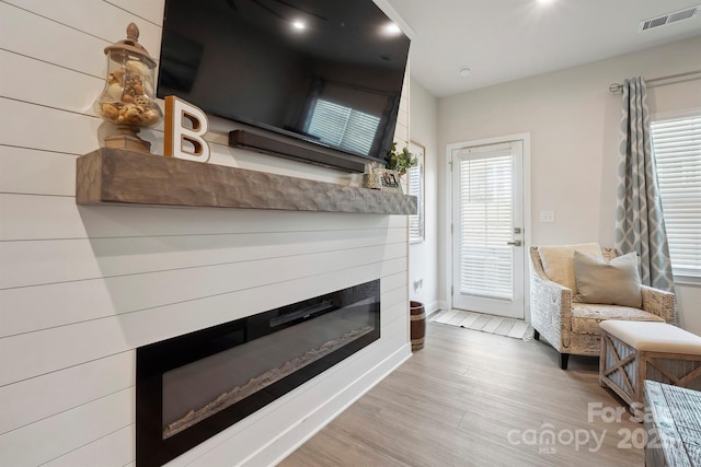 sitting room featuring visible vents, baseboards, a glass covered fireplace, and wood finished floors