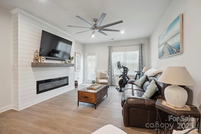 living area featuring a ceiling fan, baseboards, a glass covered fireplace, and wood finished floors