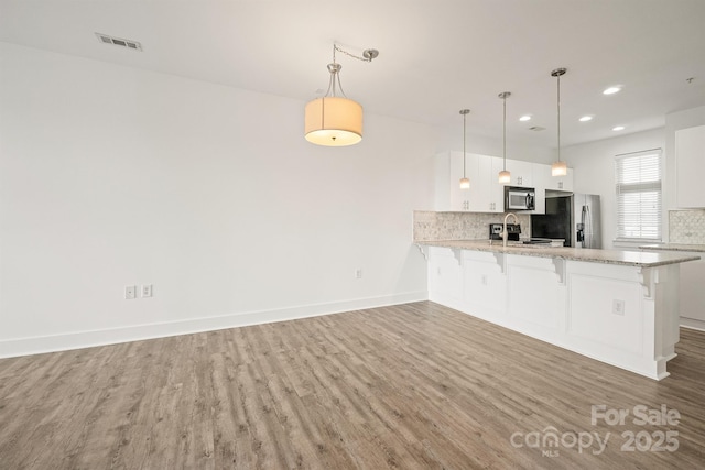 1101 W 1st St Unit 408, Charlotte, NC 28202 - kitchen featuring stainless steel appliances, wood finished floors, a peninsula, a kitchen bar, and tasteful backsplash