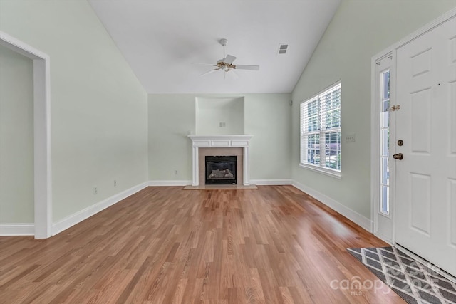 unfurnished living room featuring lofted ceiling, light wood-type flooring, ceiling fan, a fireplace with flush hearth, and baseboards