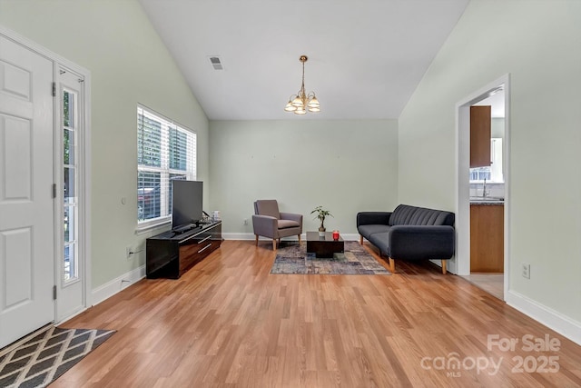 entryway with vaulted ceiling, a chandelier, light wood-type flooring, and baseboards