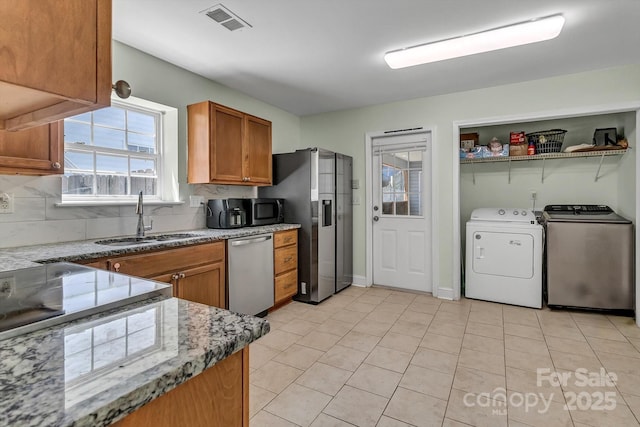 kitchen with appliances with stainless steel finishes, a sink, brown cabinets, washer and clothes dryer, and decorative backsplash