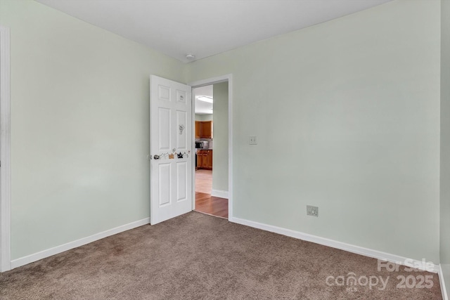 unfurnished room featuring dark carpet and baseboards