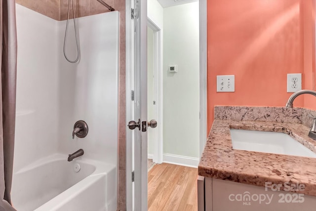 bathroom with washtub / shower combination, wood finished floors, vanity, and baseboards