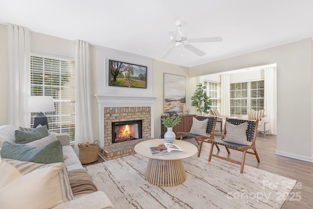living area featuring a brick fireplace, a ceiling fan, baseboards, and wood finished floors