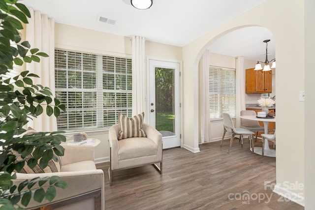 living area featuring visible vents, arched walkways, wood finished floors, baseboards, and a notable chandelier
