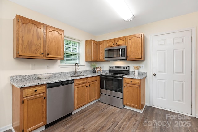 kitchen featuring brown cabinets, light stone countertops, appliances with stainless steel finishes, a sink, and dark wood finished floors