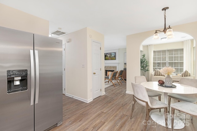 dining area featuring visible vents, arched walkways, a fireplace, baseboards, and light wood-style floors