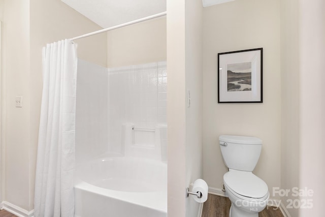 bathroom featuring baseboards, wood finished floors, shower / bath combination with curtain, and toilet