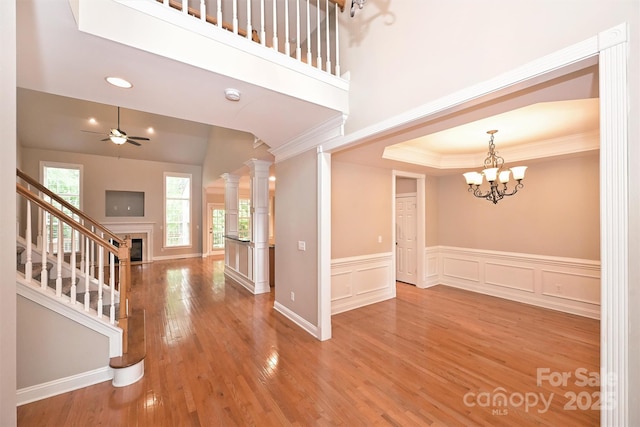 foyer with ornamental molding, stairs, wainscoting, light wood-style floors, and ceiling fan with notable chandelier