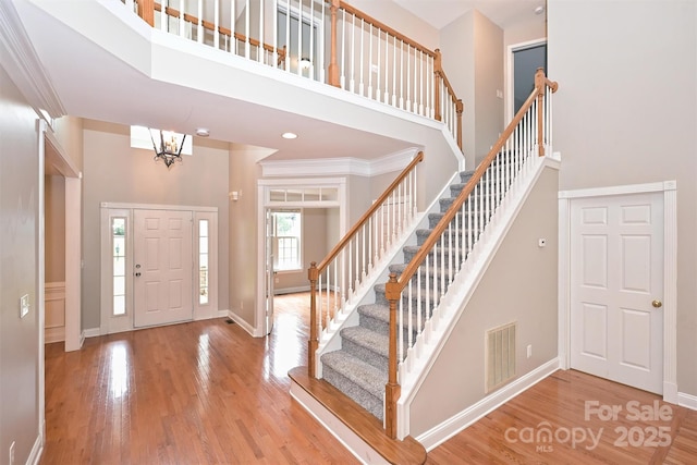 entrance foyer featuring baseboards, visible vents, wood finished floors, and a towering ceiling