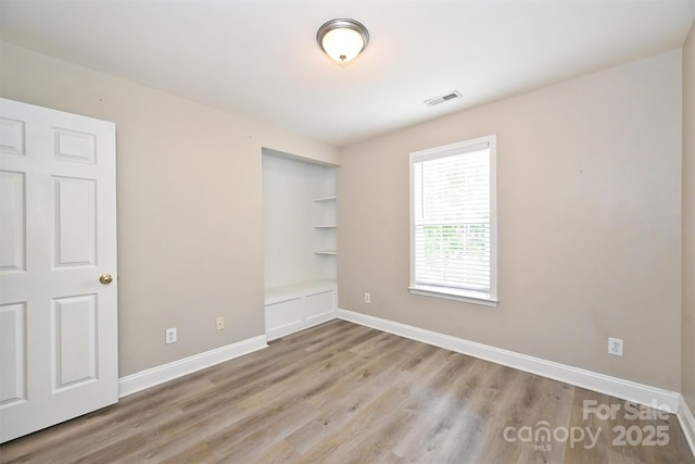 unfurnished room with visible vents, baseboards, wood finished floors, and built in shelves