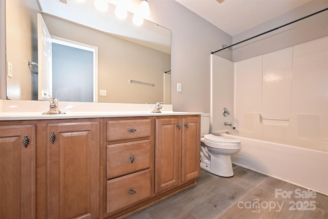 bathroom featuring double vanity, a sink, wood finished floors, and toilet