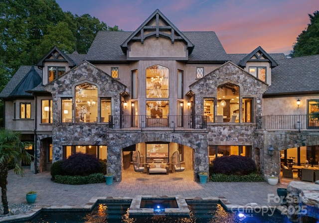 172 Tennessee Cir, Mooresville, NC 28117 - back of house at dusk with a balcony, stone siding, a patio area, and an outdoor living space