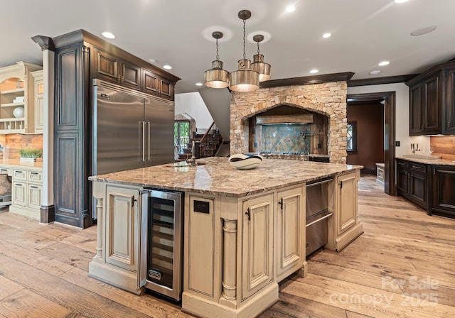 172 Tennessee Cir, Mooresville, NC 28117 - kitchen featuring beverage cooler, cream cabinetry, light wood-style flooring, a kitchen island with sink, and light stone counters