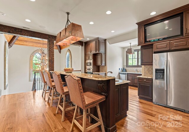 172 Tennessee Cir, Mooresville, NC 28117 - kitchen featuring appliances with stainless steel finishes, light wood-type flooring, tasteful backsplash, dark brown cabinetry, and light stone counters