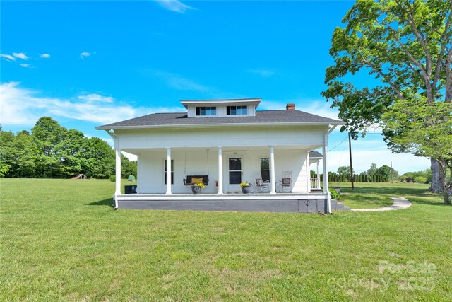 rear view of property featuring a lawn, a chimney, and covered porch