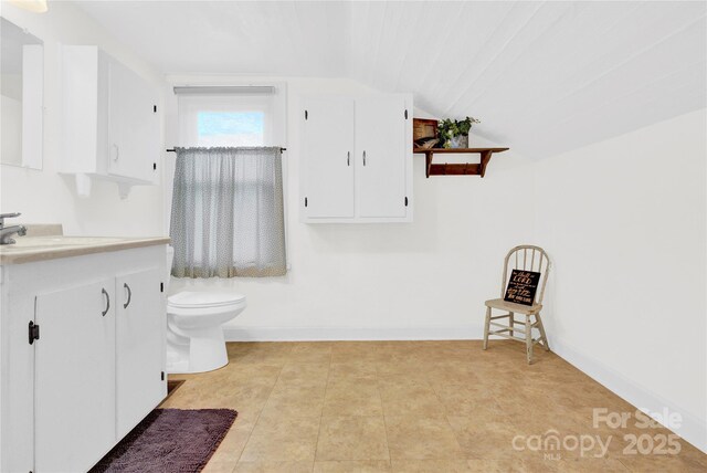 bathroom featuring vanity, baseboards, vaulted ceiling, and toilet