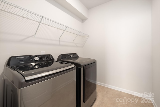 clothes washing area featuring washer and clothes dryer, baseboards, and light tile patterned floors