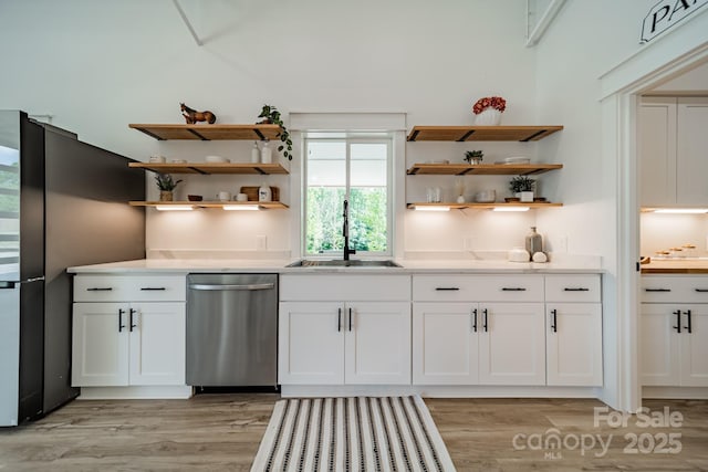 kitchen featuring white cabinets, open shelves, a sink, light wood finished floors, and stainless steel dishwasher