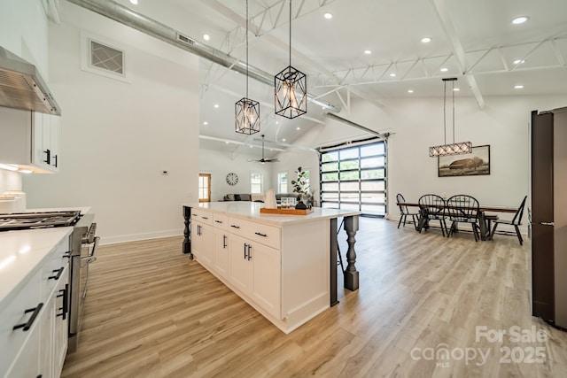 kitchen featuring white cabinets, stainless steel stove, wall chimney exhaust hood, open floor plan, and beamed ceiling