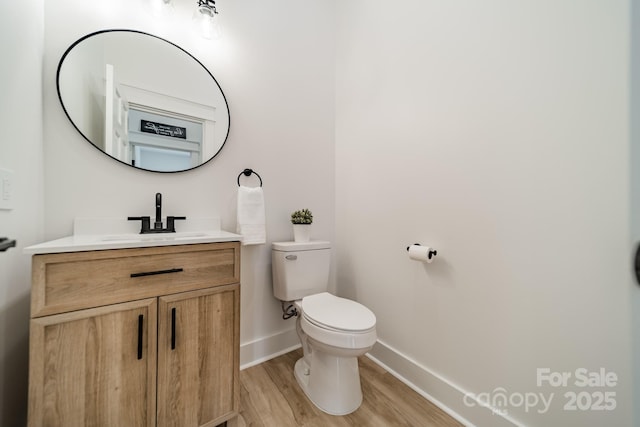 half bathroom with vanity, baseboards, toilet, and wood finished floors