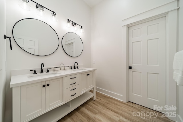 full bath featuring double vanity, a sink, baseboards, and wood finished floors
