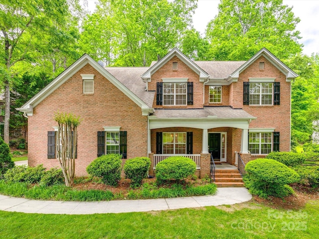 view of front of property featuring a porch, brick siding, a shingled roof, and a front yard