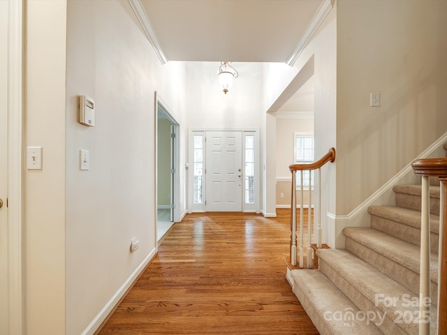 foyer with crown molding, baseboards, light wood finished floors, and stairs