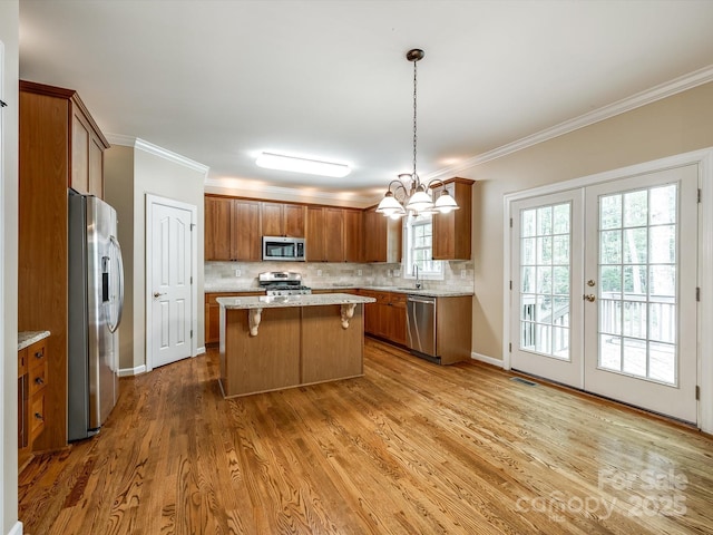kitchen featuring brown cabinetry, a kitchen island, backsplash, appliances with stainless steel finishes, and a sink