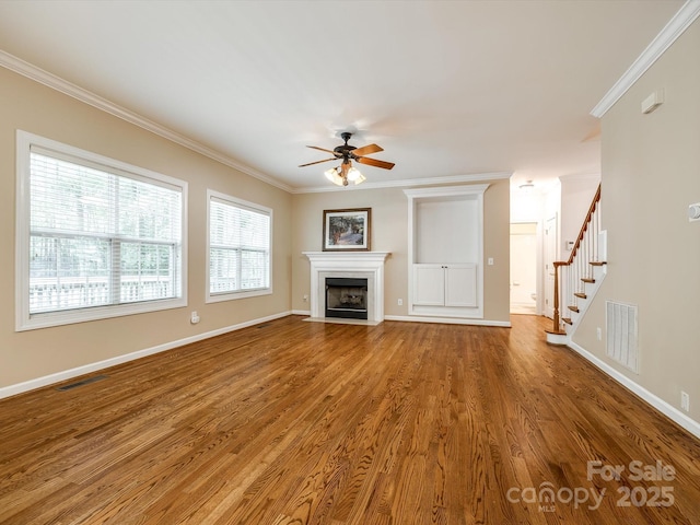 unfurnished living room featuring crown molding, a ceiling fan, visible vents, and wood finished floors