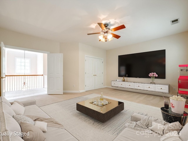 living room with ceiling fan, visible vents, light carpet, and baseboards