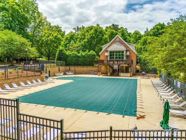 community pool with a patio, fence, a wooden deck, and stairs
