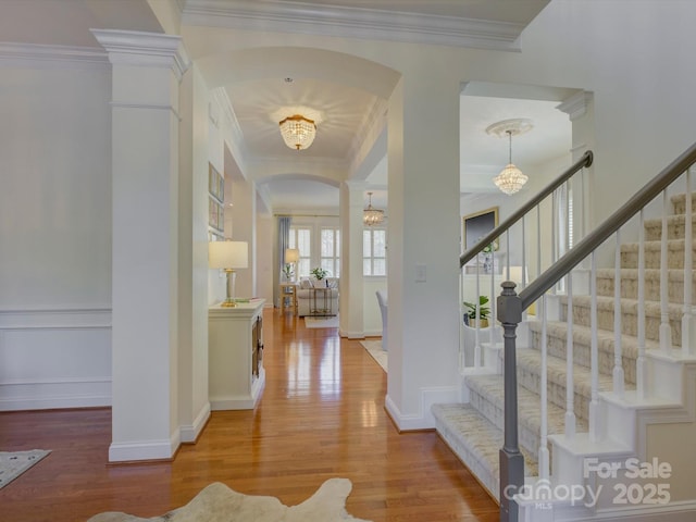 foyer with arched walkways, wood finished floors, a chandelier, ornamental molding, and stairs