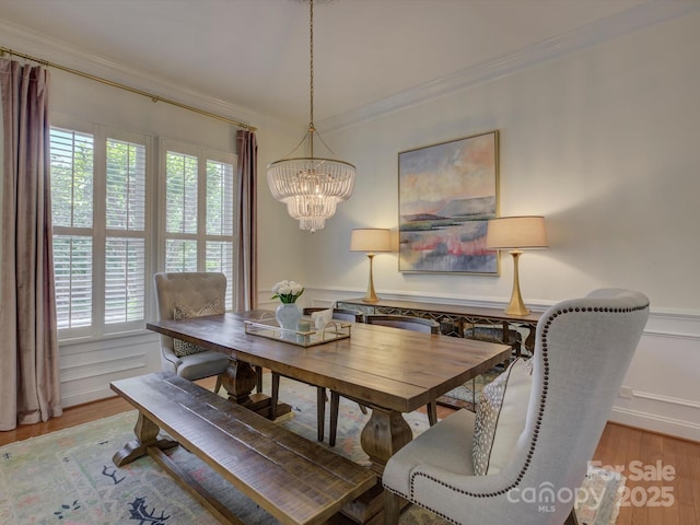 dining room with crown molding, wood finished floors, a notable chandelier, and a wainscoted wall