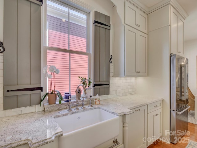 kitchen with decorative backsplash, light stone countertops, high end fridge, a sink, and light wood finished floors
