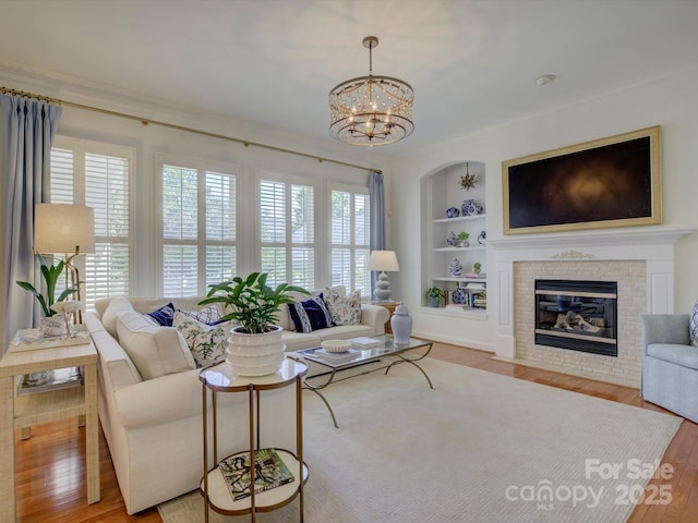 living area featuring a notable chandelier, built in features, wood finished floors, and a fireplace