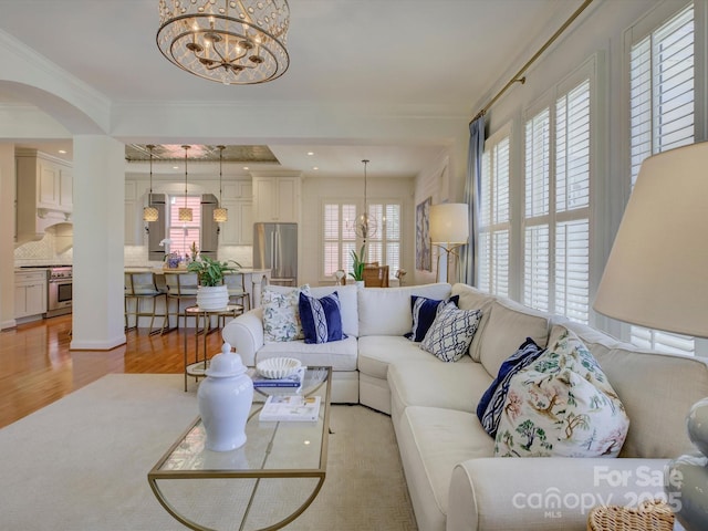 living room featuring crown molding, recessed lighting, a chandelier, arched walkways, and light wood finished floors