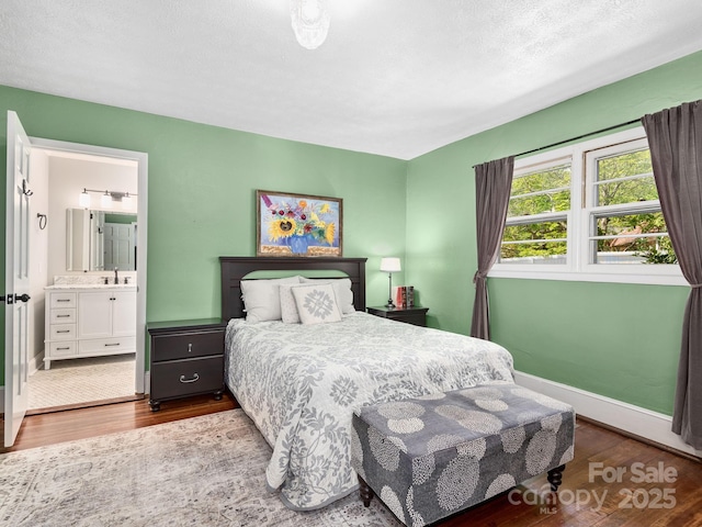 bedroom featuring wood finished floors, baseboards, a textured ceiling, a sink, and ensuite bath