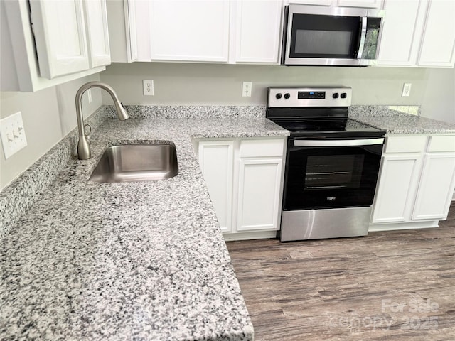 kitchen featuring appliances with stainless steel finishes, a sink, white cabinetry, light stone counters, and wood finished floors