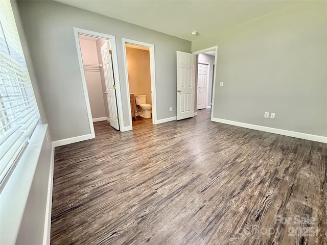 unfurnished bedroom featuring dark wood finished floors, baseboards, a walk in closet, and connected bathroom