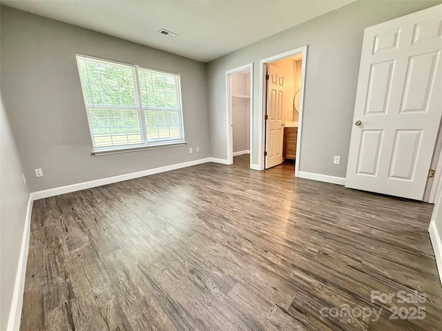 unfurnished bedroom featuring dark wood finished floors, baseboards, a spacious closet, and a closet