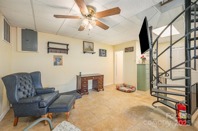 living area with baseboards, a drop ceiling, stairway, electric panel, and a ceiling fan