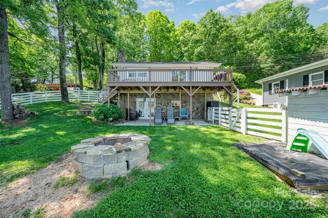 rear view of house with a lawn, an outdoor fire pit, a deck, and stone siding