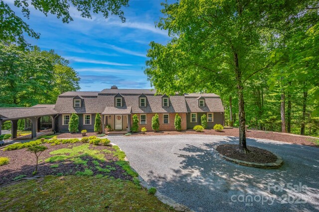 colonial inspired home with a chimney, curved driveway, a shingled roof, and a gambrel roof