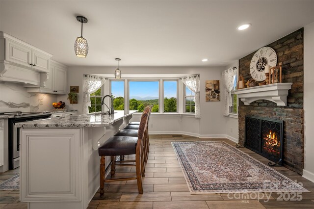 kitchen with a fireplace, baseboards, stainless steel electric stove, light stone counters, and a sink
