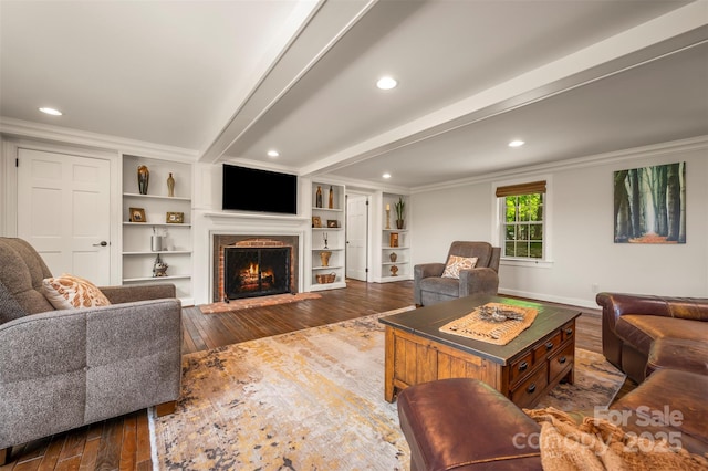 living room with ornamental molding, beamed ceiling, dark wood-style floors, a lit fireplace, and recessed lighting